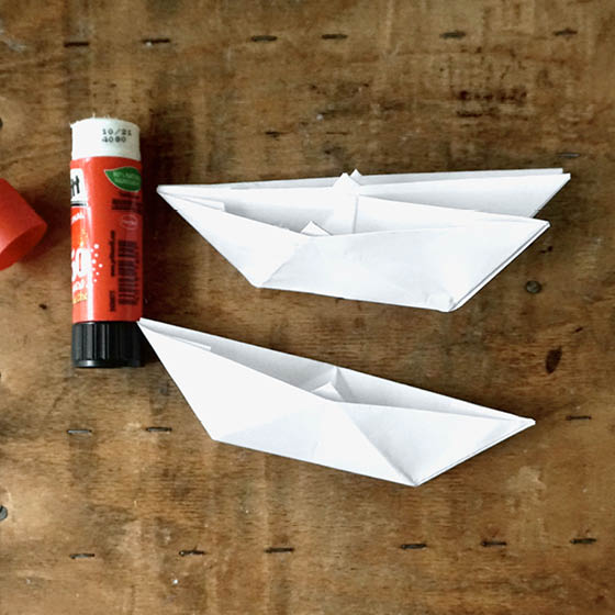 Klebestift, zwei aufeinander geklebte Papierboote, ein weiteres Papierboot