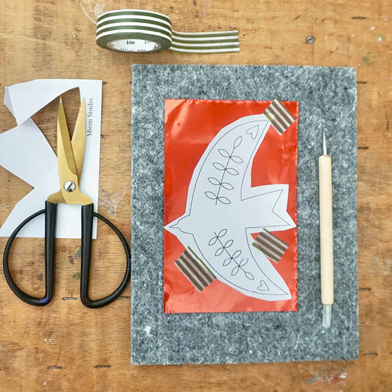 Arbeitsplatz: Prägefolie auf Filzmatte, darauf eine Vorlage (Vogel). prägenadel Schere, Washi-Tape