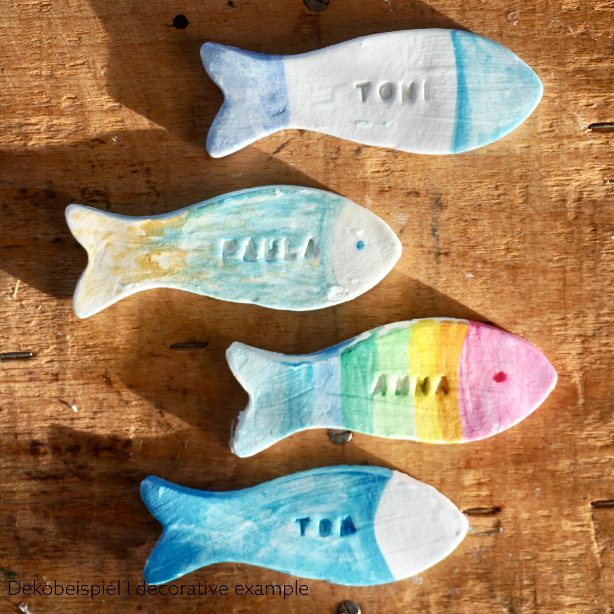 Platzkarten aus Modelliermasse in Fischform. Anwendungsbeispiel: 4 bunt bemalte Fische mit eingestempelten Namen