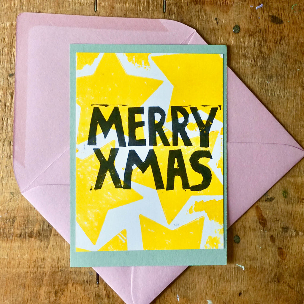von Hand gedruckte Weihnachtskarte: Rosa Umschlag, grüne Karte als Basis, Weiße arte mit aufgedruckten gelben Sternen und Schriftzug MERRY XMAS