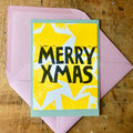 von Hand gedruckte Weihnachtskarte: Rosa Umschlag, grüne Karte als Basis, Weiße arte mit aufgedruckten gelben Sternen und Schriftzug MERRY XMAS