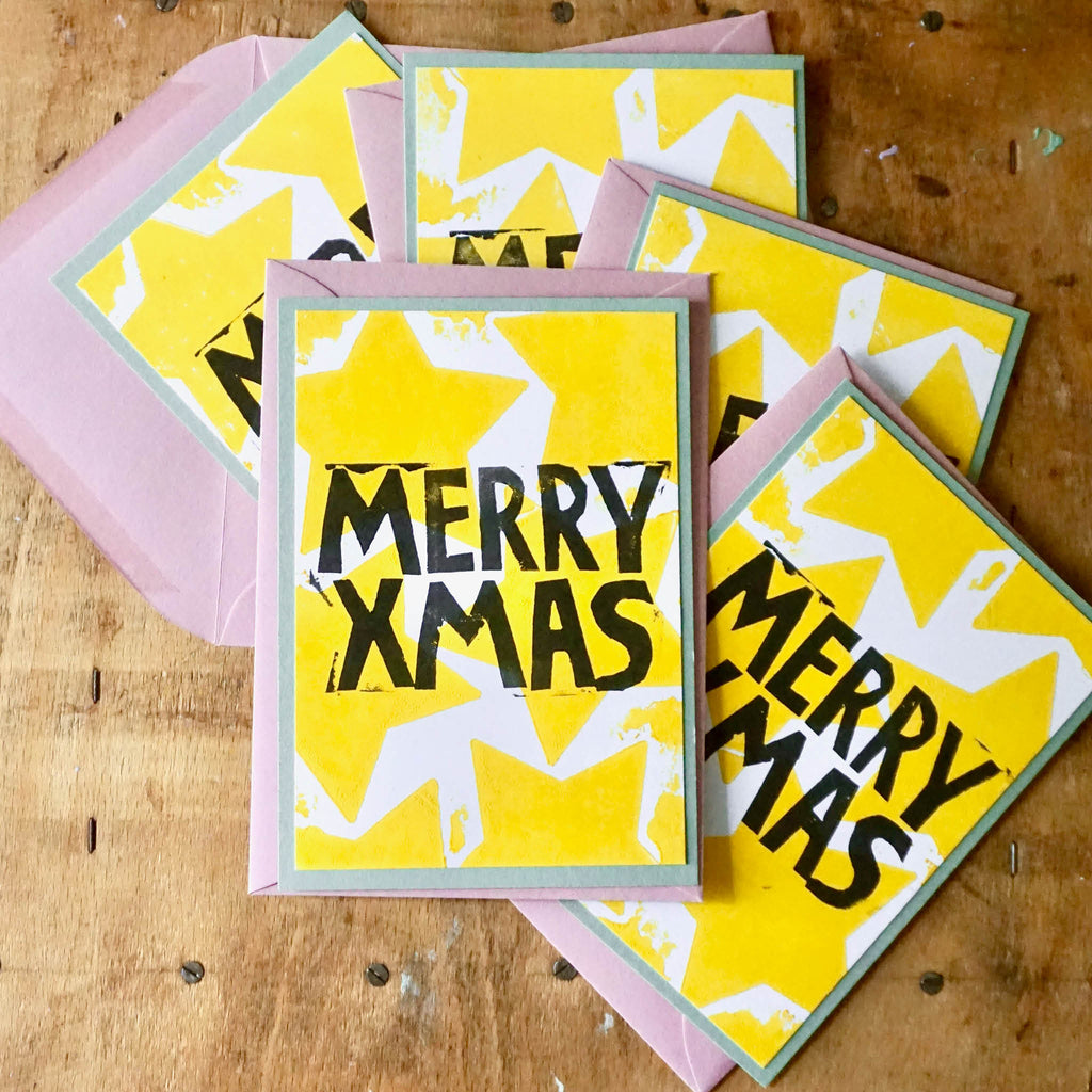 von Hand gedruckte Weihnachtskarten: Rosa Umschlag, grüne Karte als Basis, Weiße arte mit aufgedruckten gelben Sternen und Schriftzug MERRY XMAS